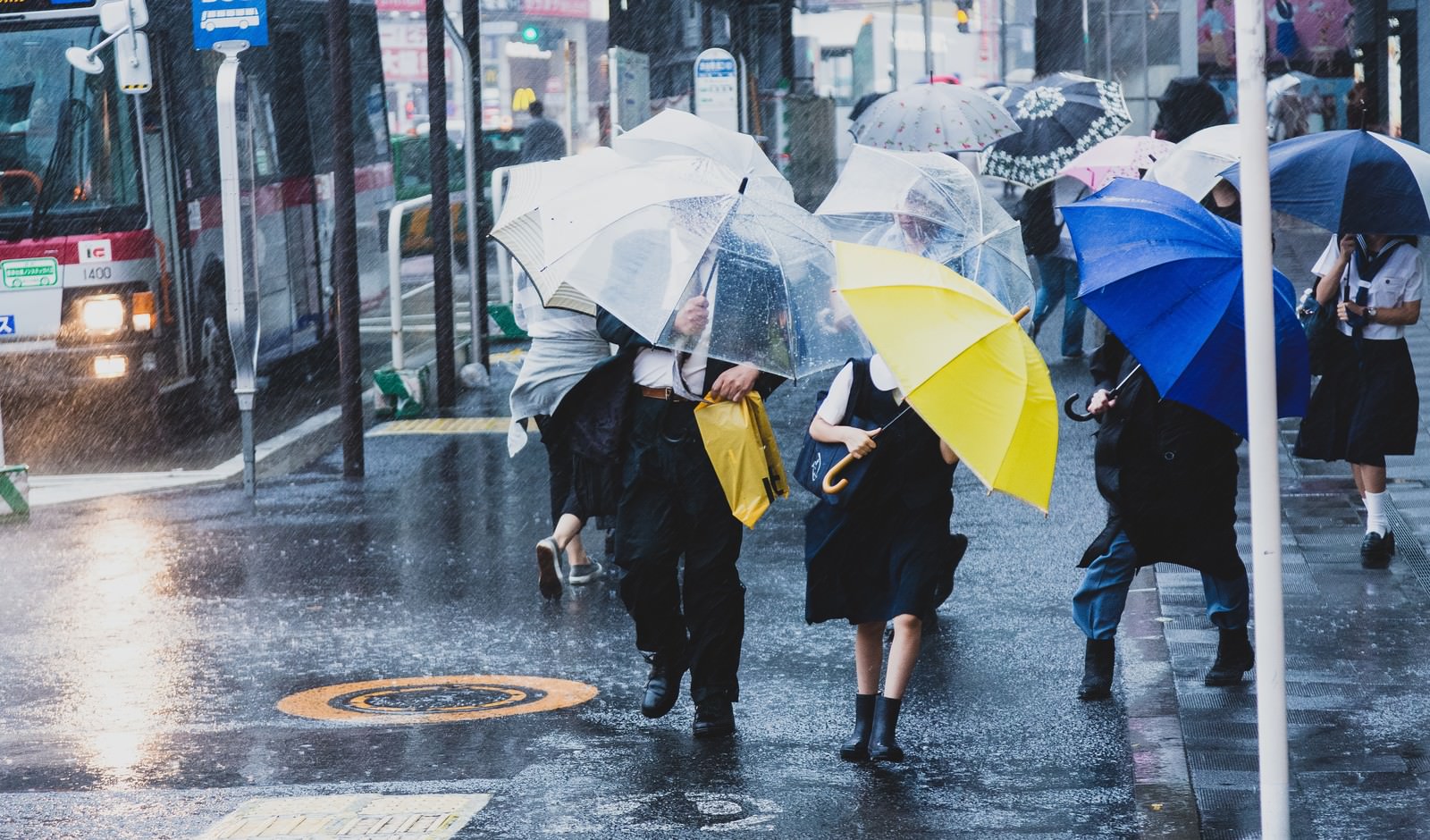 「台風で突風が吹く駅前と必死に傘をさす人々」の写真