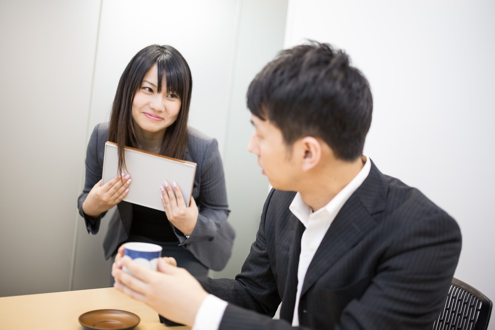 「「お茶どうぞ」と意味深な笑顔で打ち合わせに茶々を入れる小悪魔女子」の写真［モデル：大川竜弥 Lala］