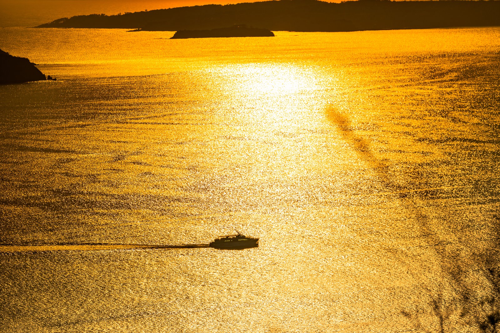 「黄金色に輝く夕刻の海と渡し船」の写真