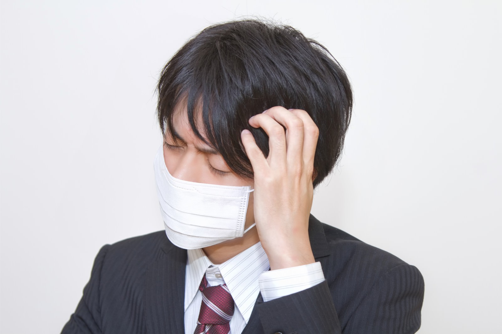 「マスクをして頭をかかえるスーツの男性 | フリー素材のぱくたそ」の写真［モデル：Tsuyoshi.］
