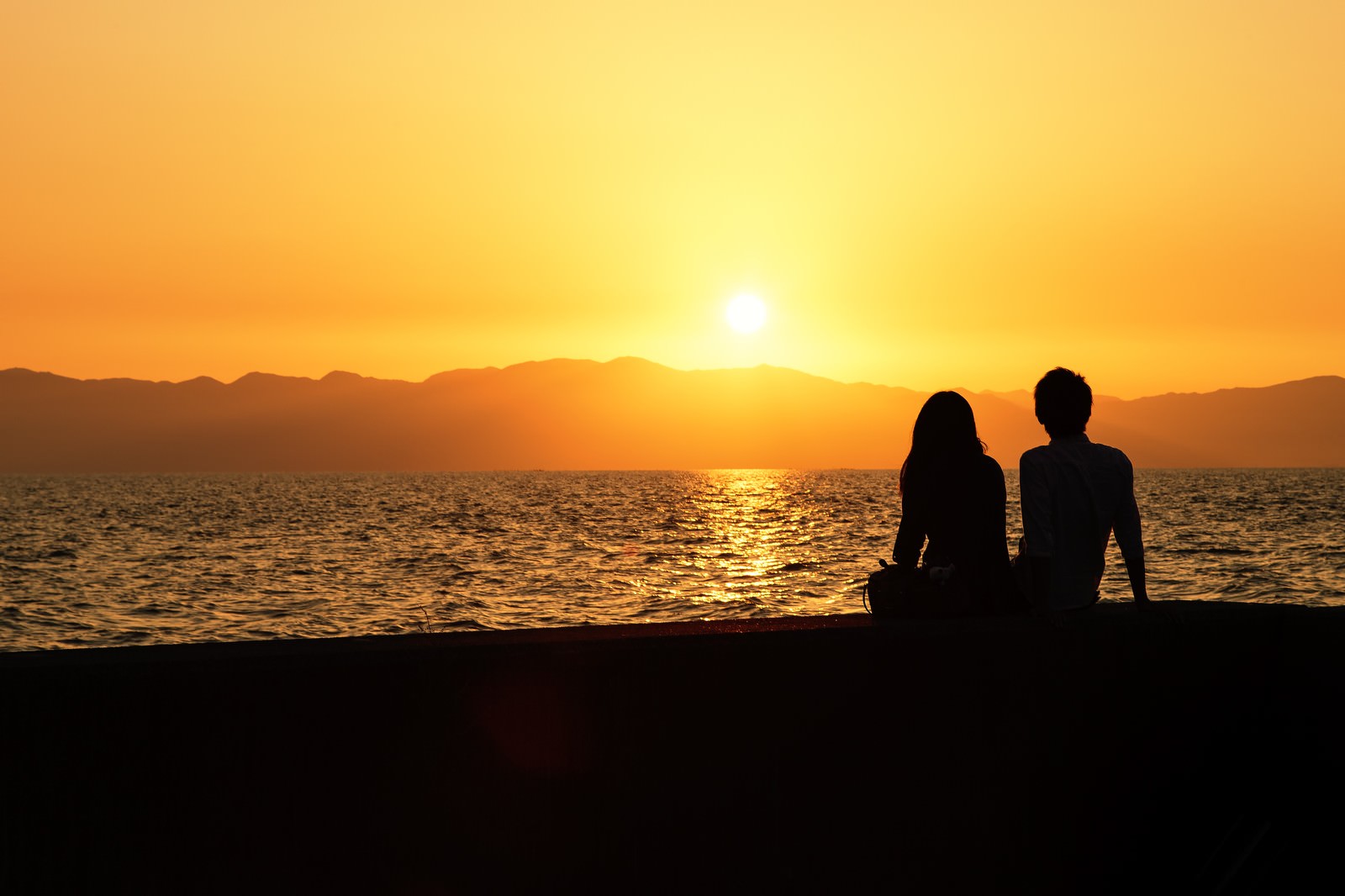 海沿いの夕焼けとカップルのシルエットの写真 画像 フリー素材 ぱくたそ