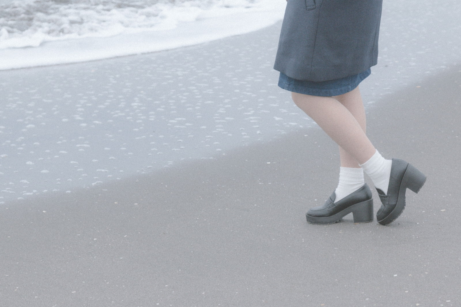 「波打ち際でたたずむ女性の足元」の写真