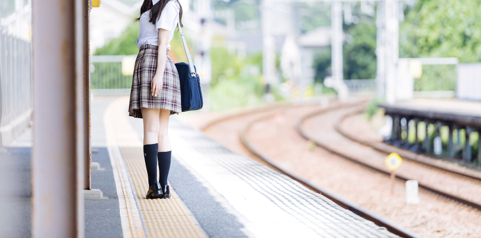 「誰もいない駅のホームと振り返る女子高生」の写真［モデル：石投げて美奈代］
