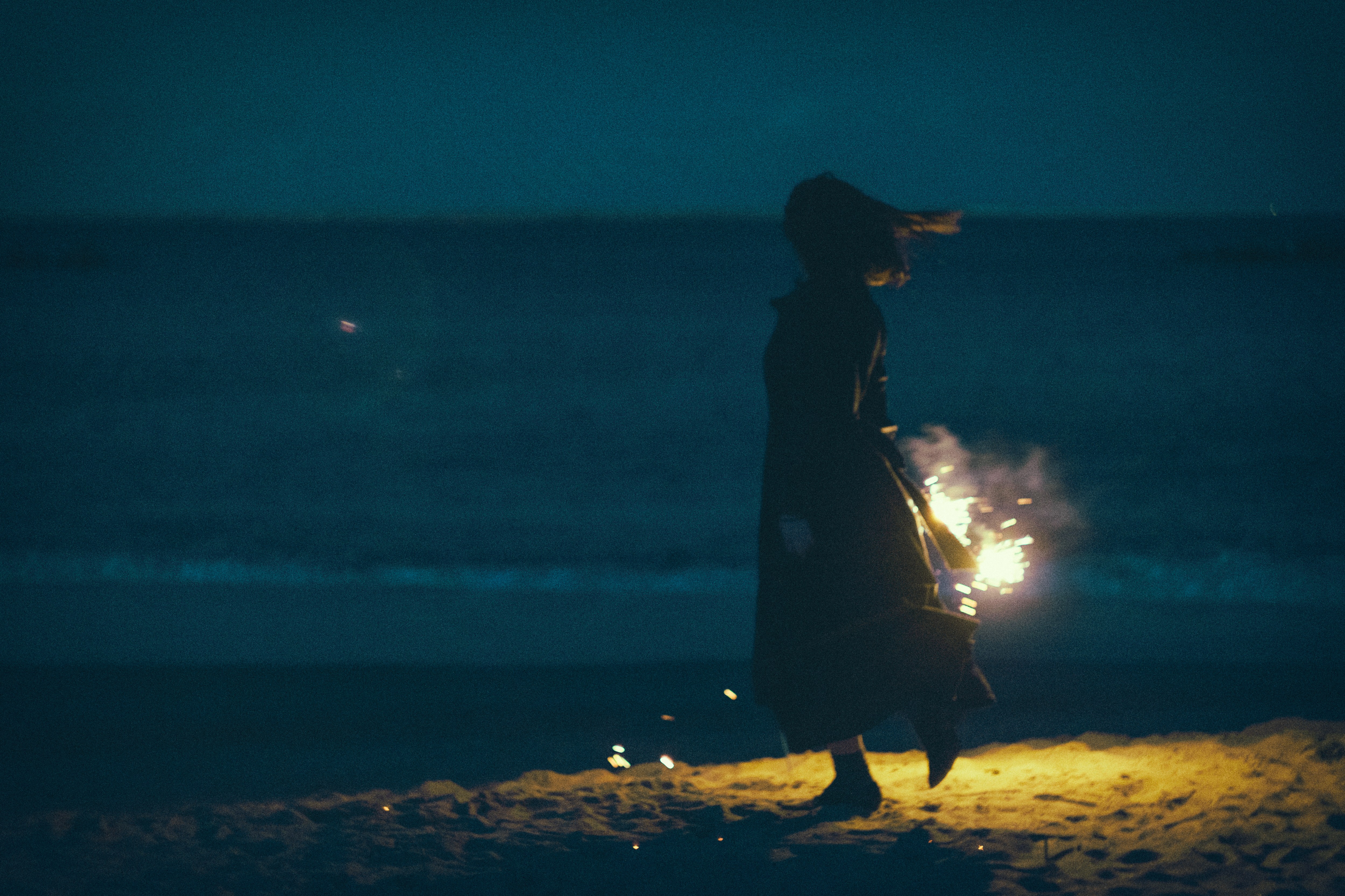 夜の浜辺で手持ち花火と女性のシルエットの写真素材 ぱくたそ