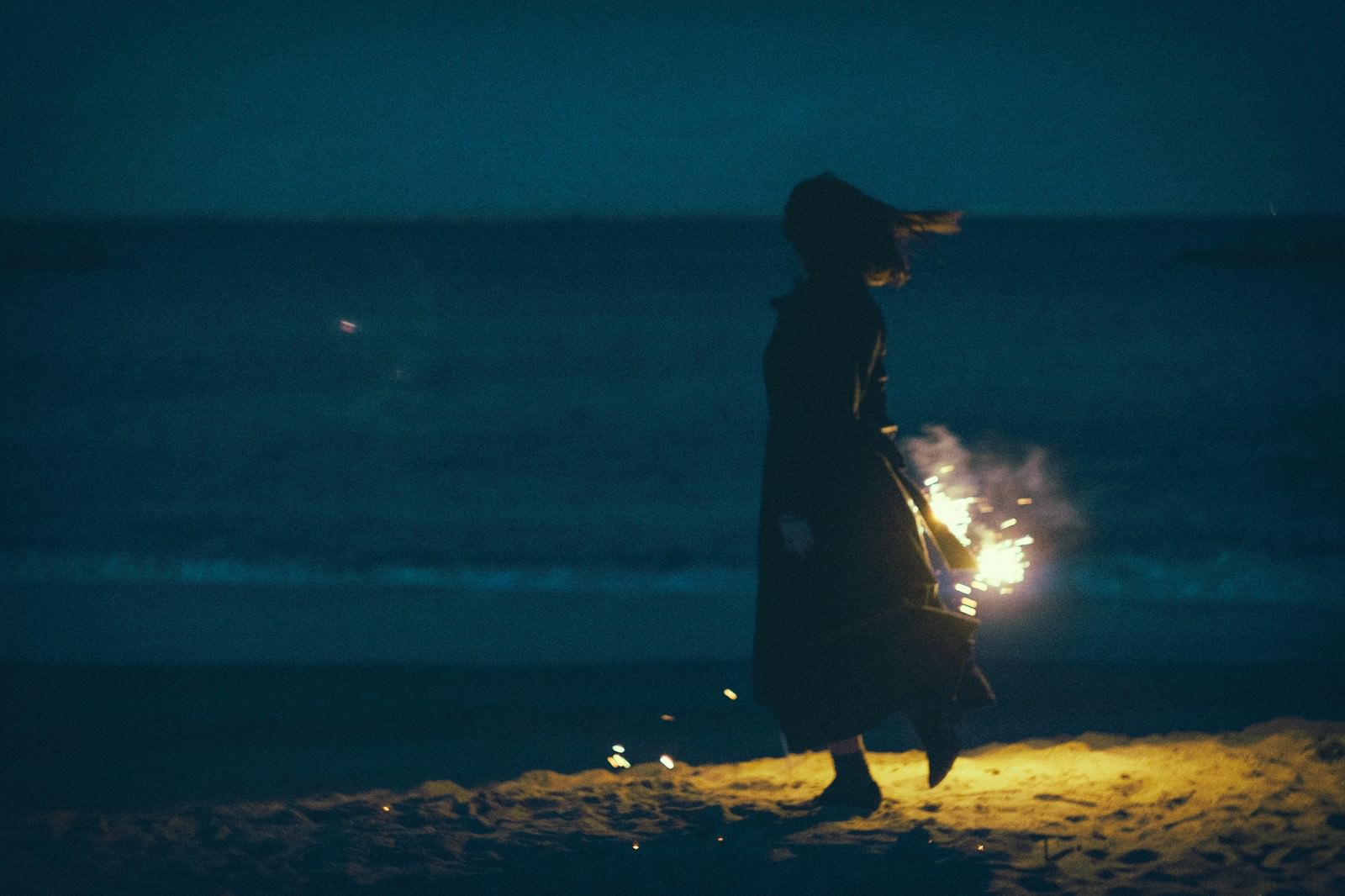 夜の浜辺で手持ち花火と女性のシルエットの写真 画像 フリー素材 ぱくたそ