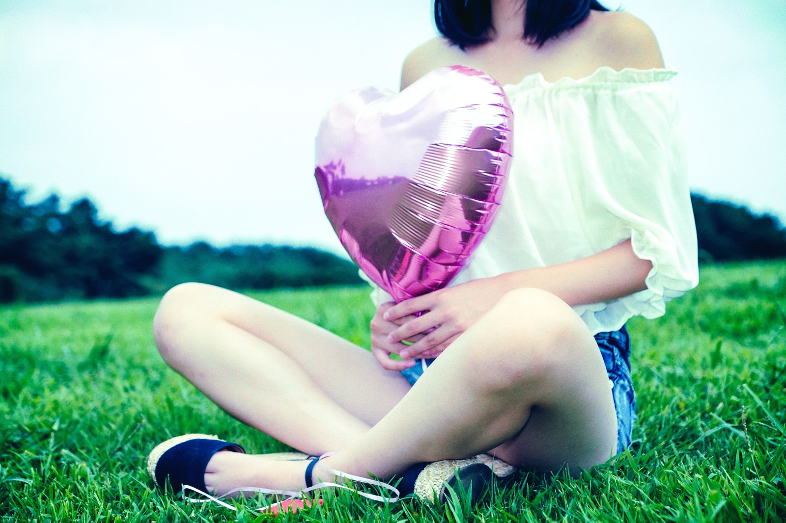 「芝生の上でハートの風船を持って座る女子 | フリー素材のぱくたそ」の写真