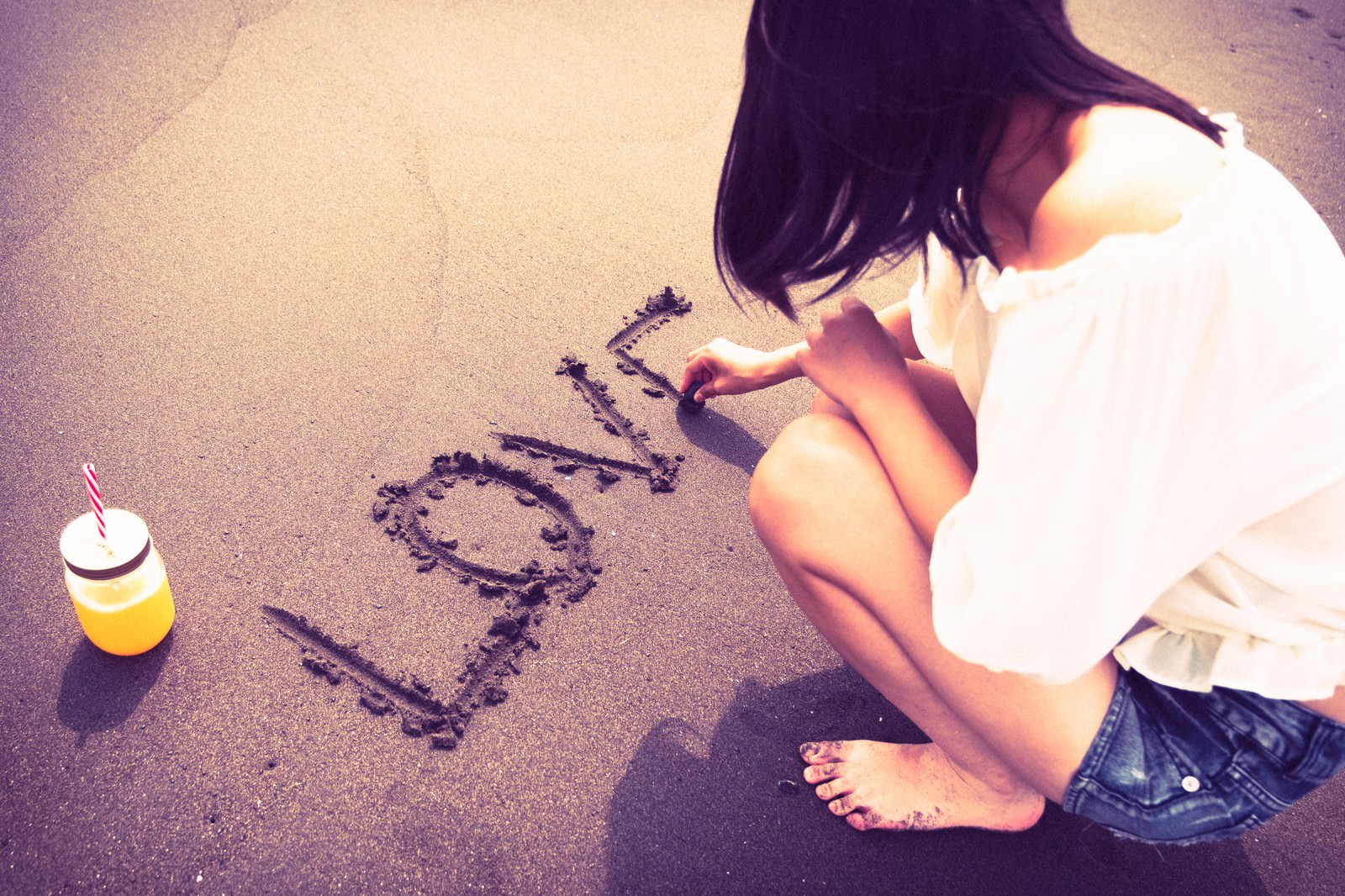 「砂の上にLOVEと文字を書く女性のうしろ姿」の写真