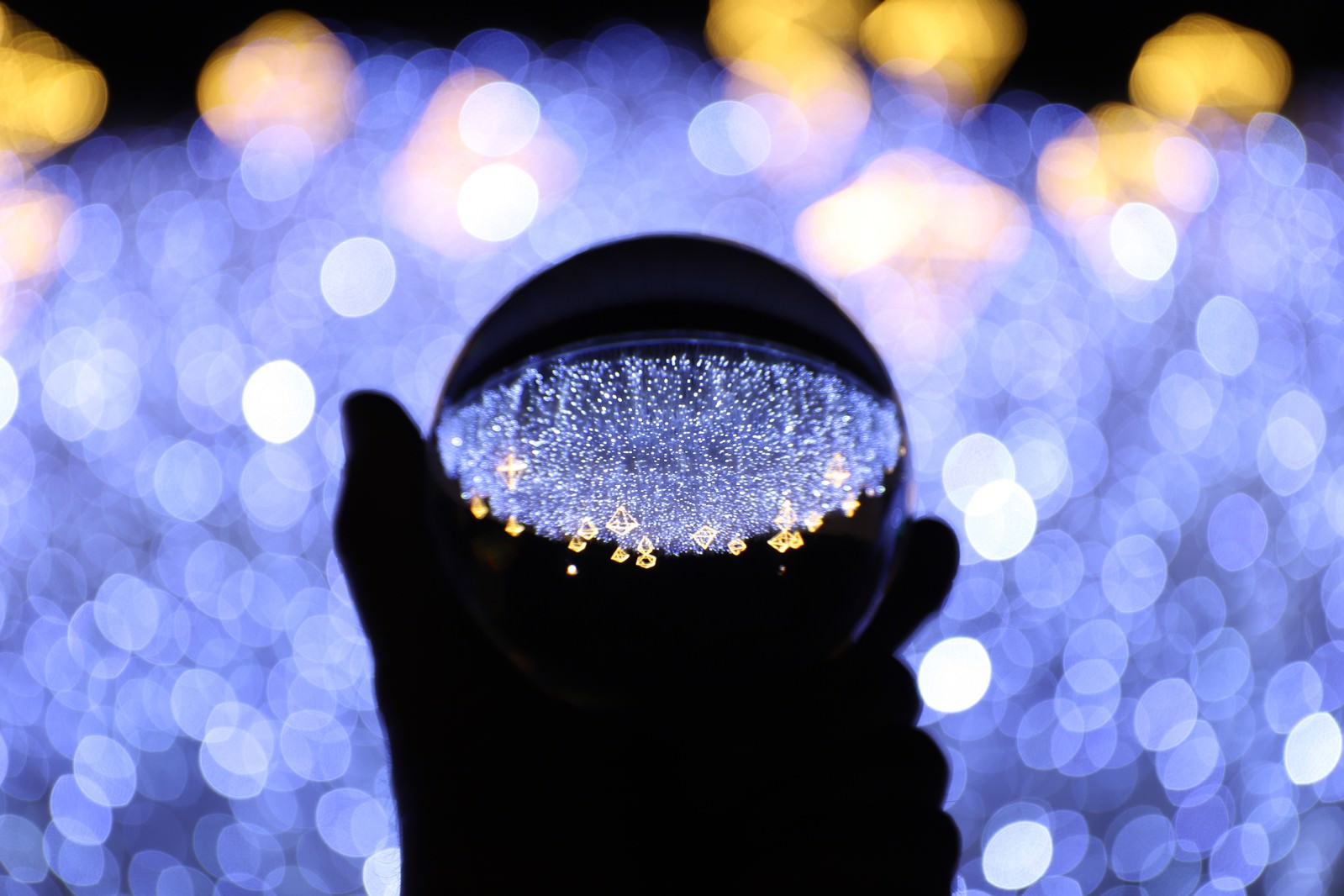 「手に持つガラス玉に写り込むイルミネーション（神戸ルミナリエ）」の写真