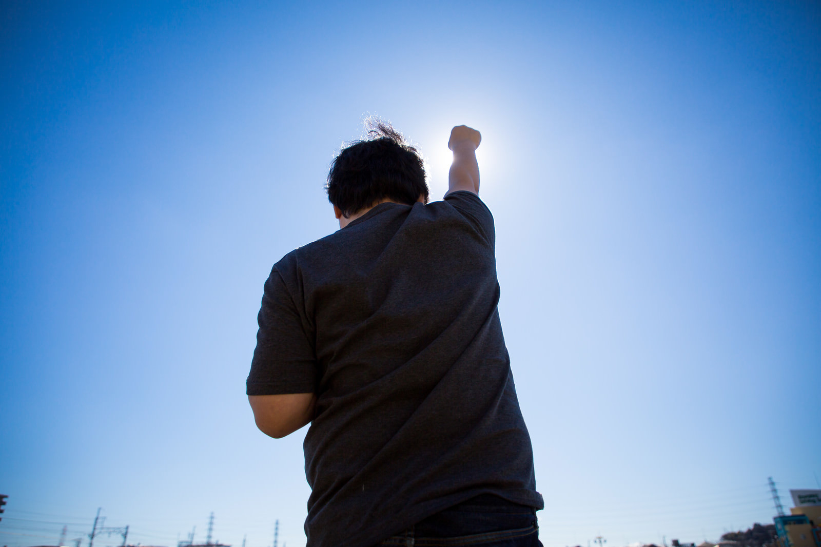 「太陽に向かって拳を高々とあげる後ろ姿」の写真［モデル：段田隼人］