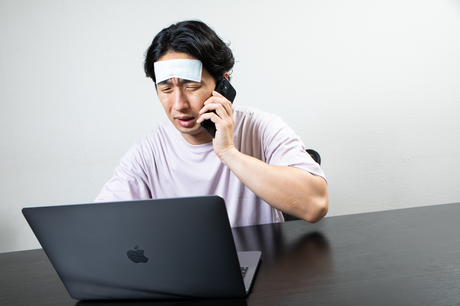 「頭を冷やしながら仕事する過労の男性」の写真［モデル：大川竜弥］