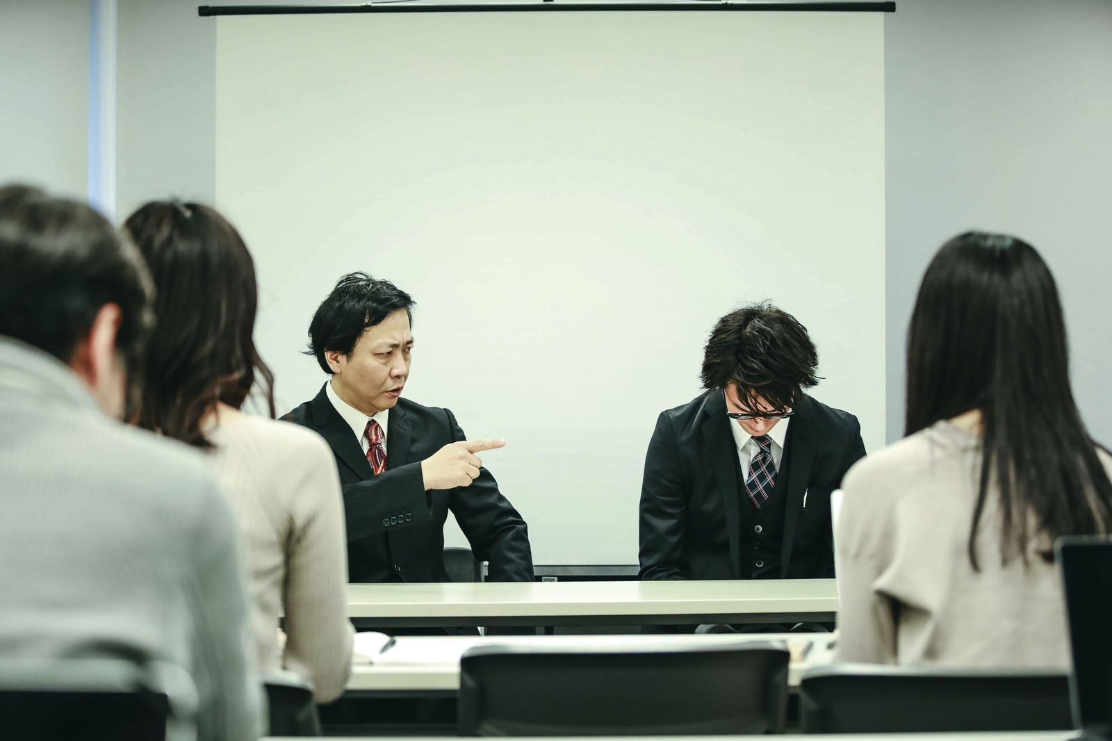 「記者会見中に役員にダメ出しされる広報」の写真［モデル：のせさん 村田裕章］