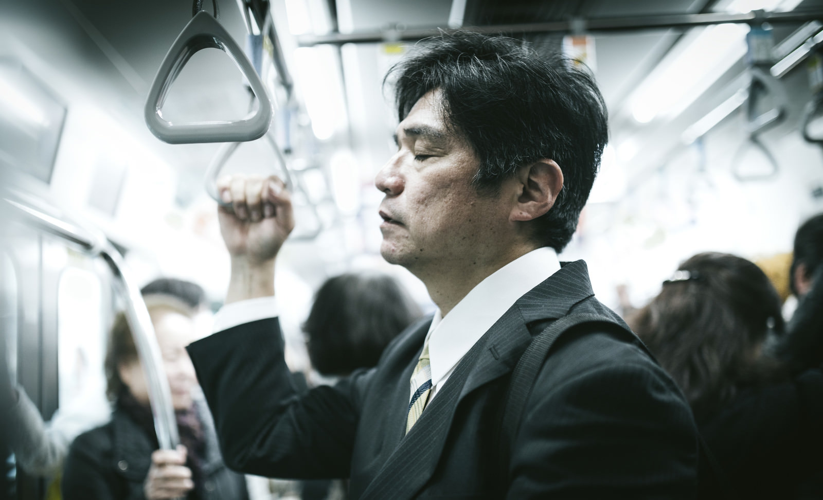 「電車の中で、立ったまま寝る中年男性」の写真