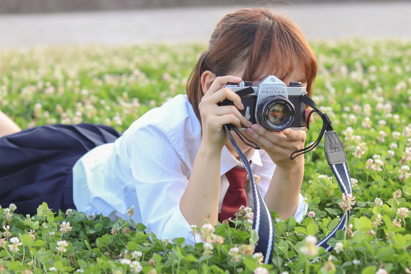 草原にうつ伏せてカメラを構える女子高生の写真素材 ぱくたそ