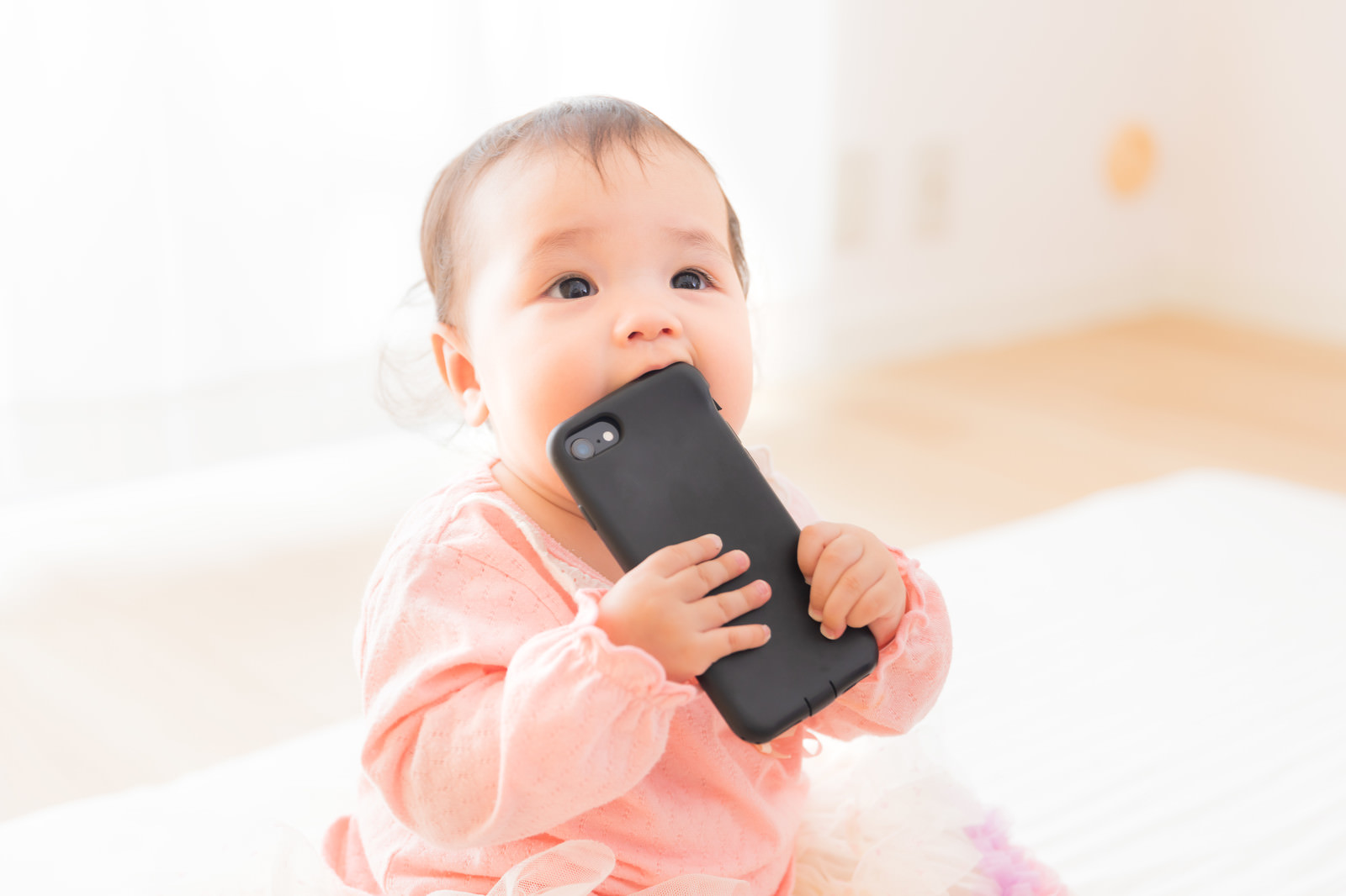 「スマートフォンを口に入れてしまう赤ちゃん」の写真［モデル：めぐな］