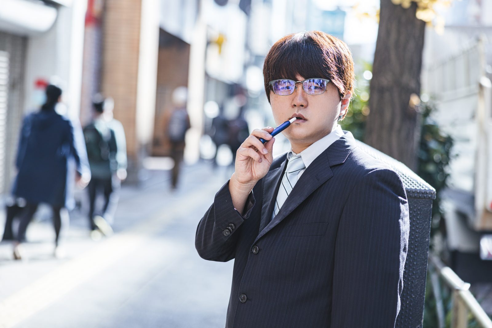 「「ここで煙草は吸わないでもらえますか」と言われて不機嫌そうな会社員 | フリー素材のぱくたそ」の写真［モデル：はしも。］