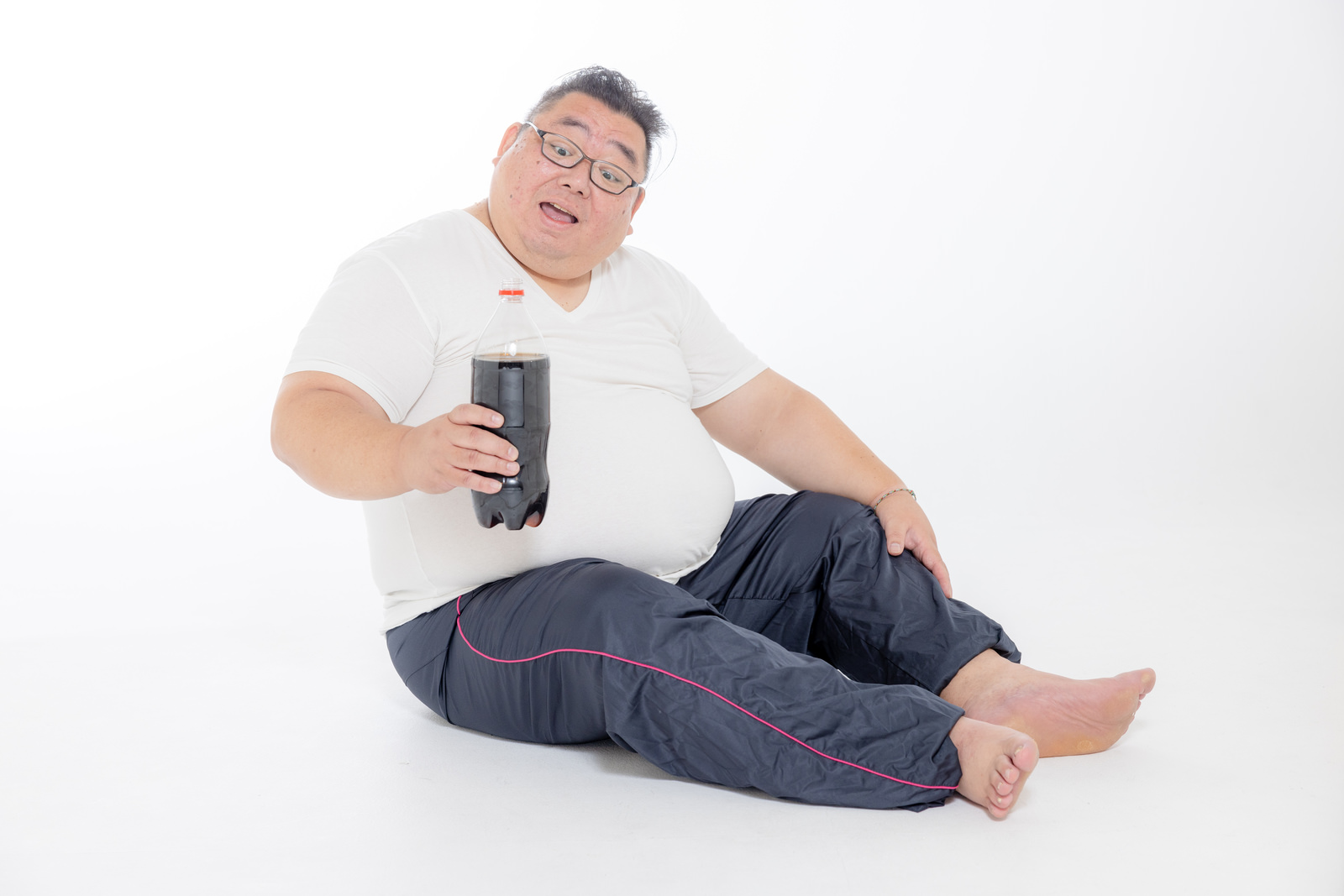 「炭酸ジュースを片手に座り込む膨よかな男性 | フリー素材のぱくたそ」の写真［モデル：ダルマ親方］