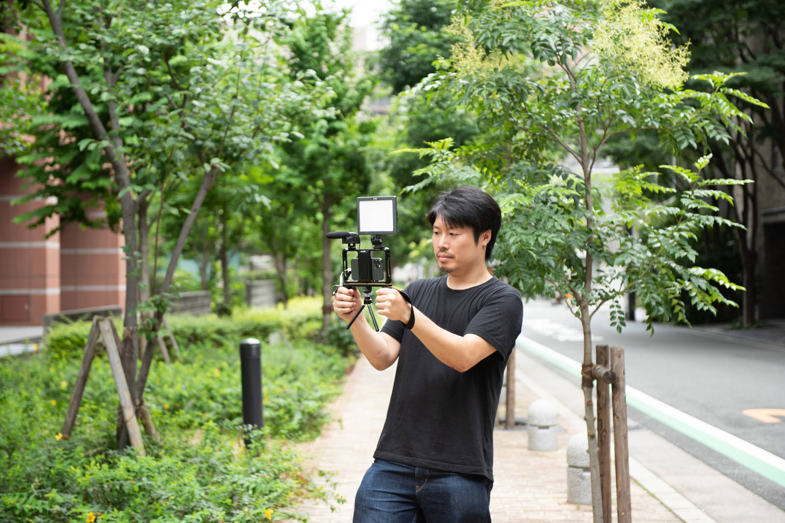 「屋外ではスマートフォンを使ってムービー撮影をする男性カメラマン | フリー素材のぱくたそ」の写真［モデル：瀧野恵太］