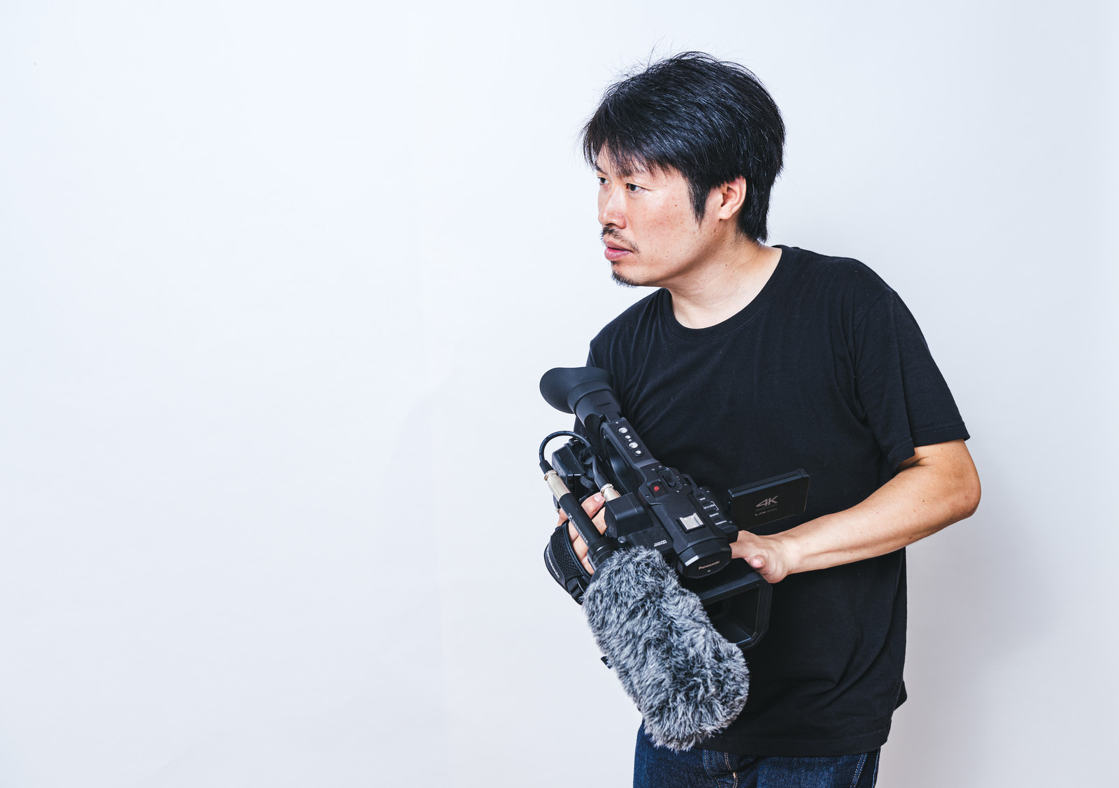 「ビデオカメラを持ってスタンバる男性カメラマン」の写真［モデル：瀧野恵太］