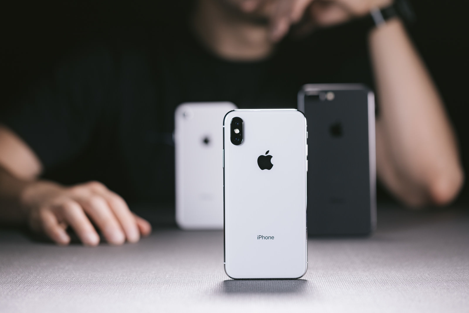 「iPhone X と iPhone 8 を並べて考える男性」の写真