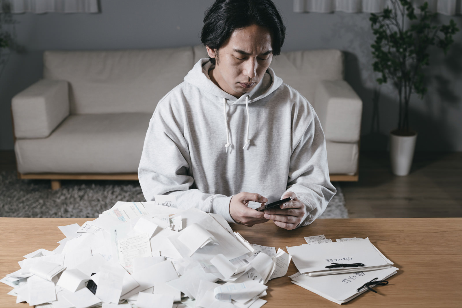 「山積みの領収書を見て現実逃避する男性 | フリー素材のぱくたそ」の写真［モデル：大川竜弥］