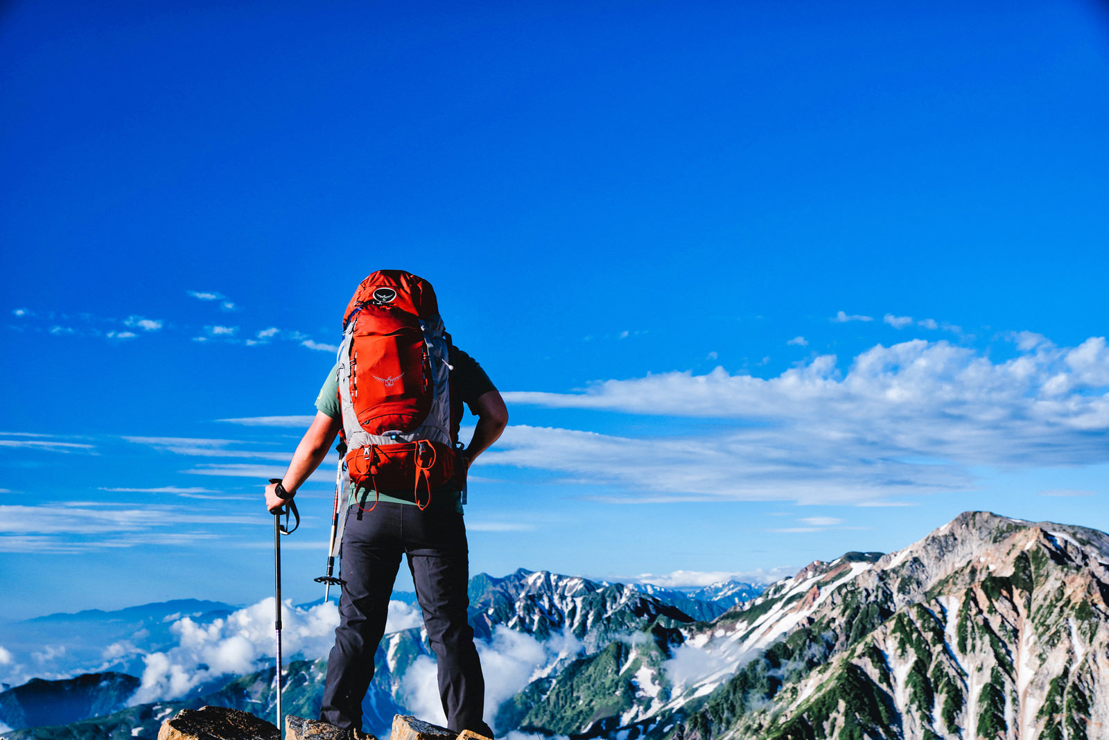 「登頂して眼下を眺める登山者の男性」の写真