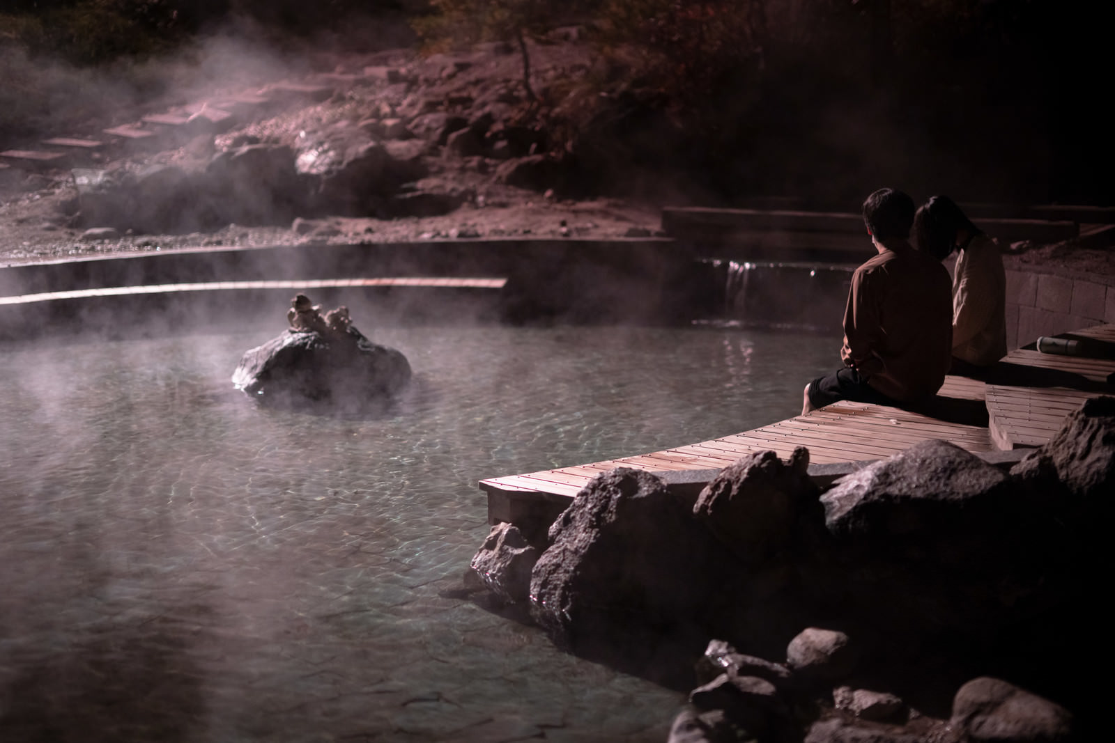 「西の河原公園で足湯に浸かる男女 | フリー素材のぱくたそ」の写真
