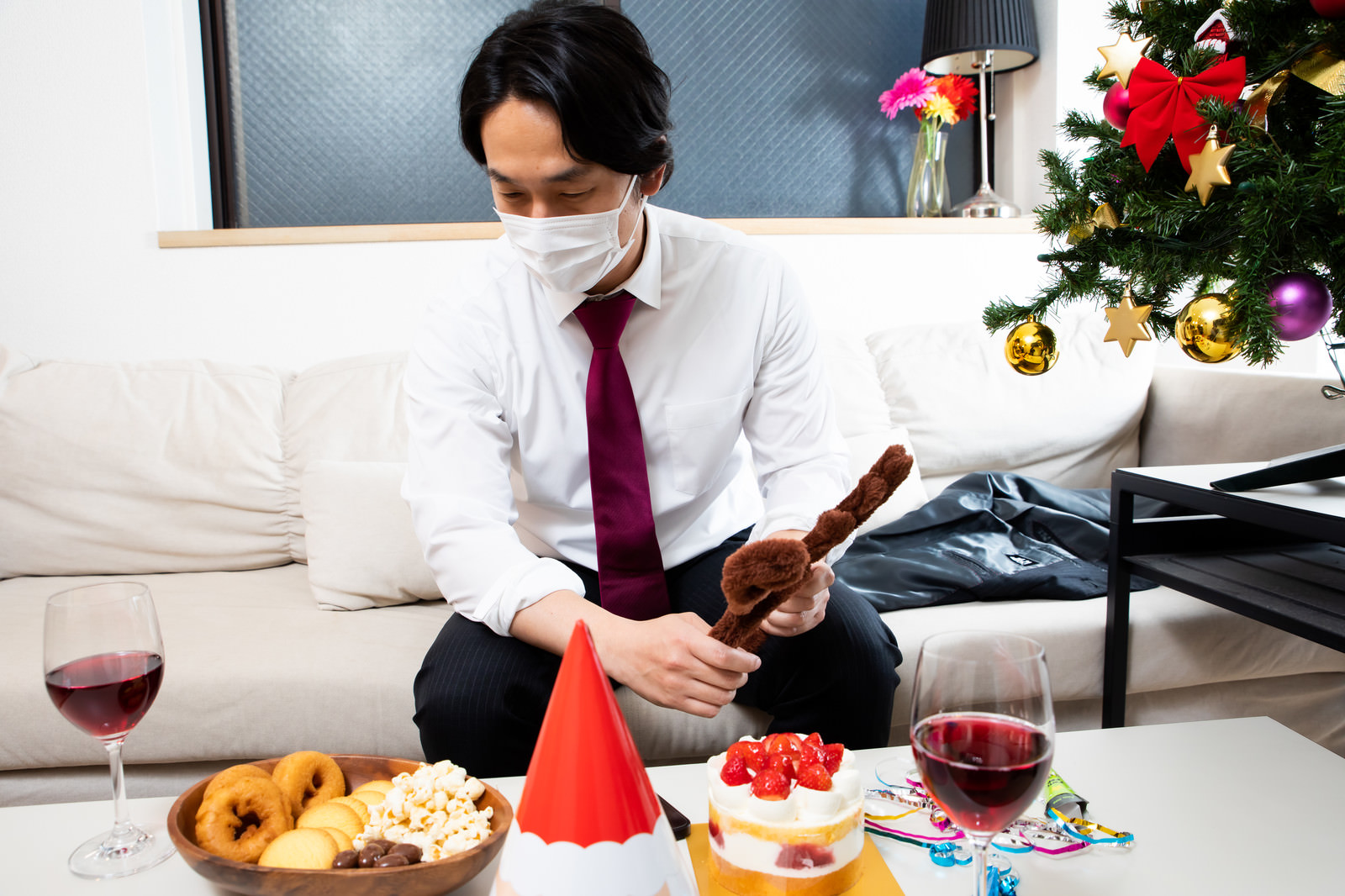 「机に並んだクリスマス用のパーティーフードとマスク着用の会社員 | フリー素材のぱくたそ」の写真［モデル：大川竜弥］