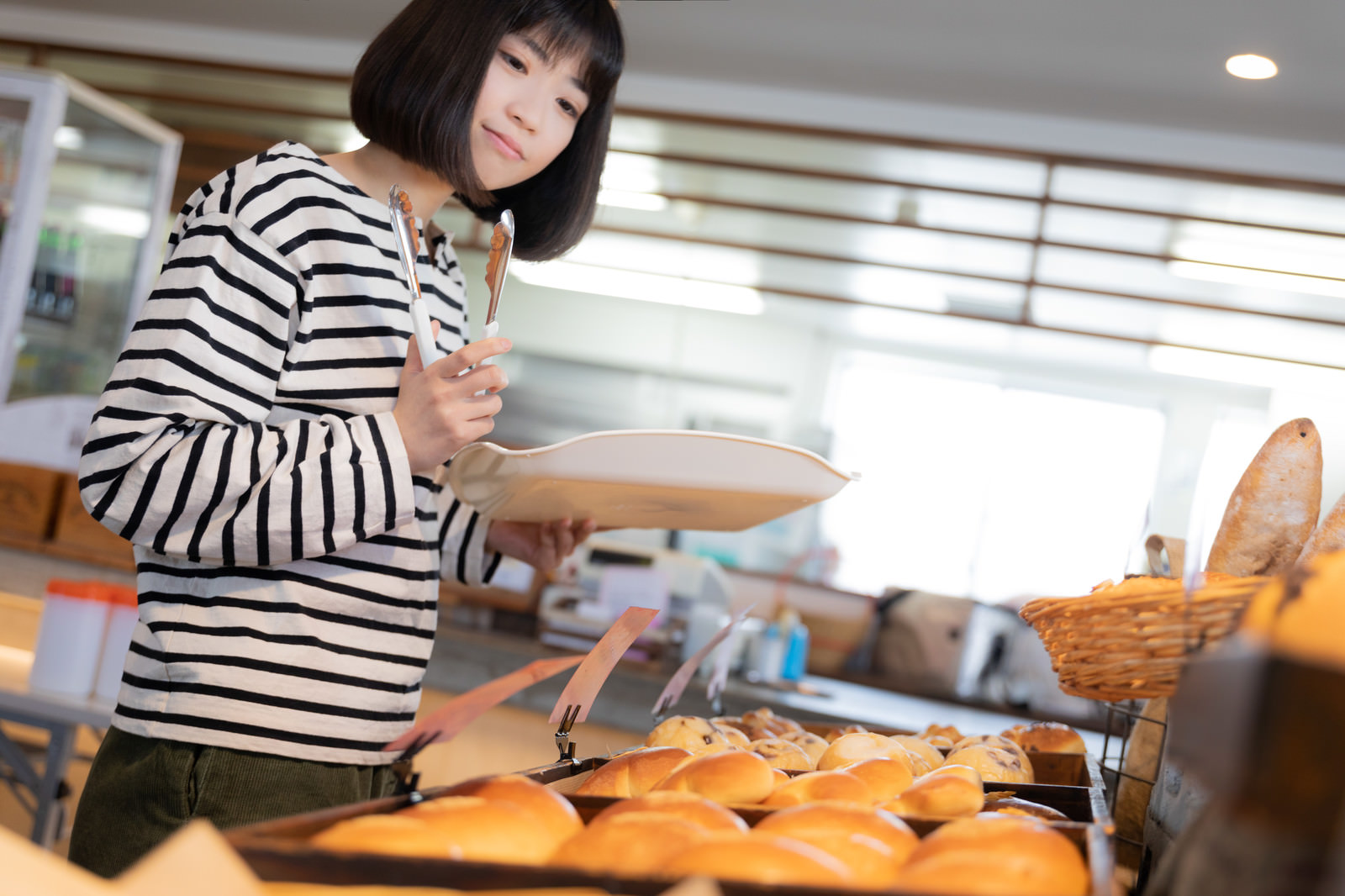 「焼きたてのパンを選ぶ女性」の写真［モデル：塩田みう］