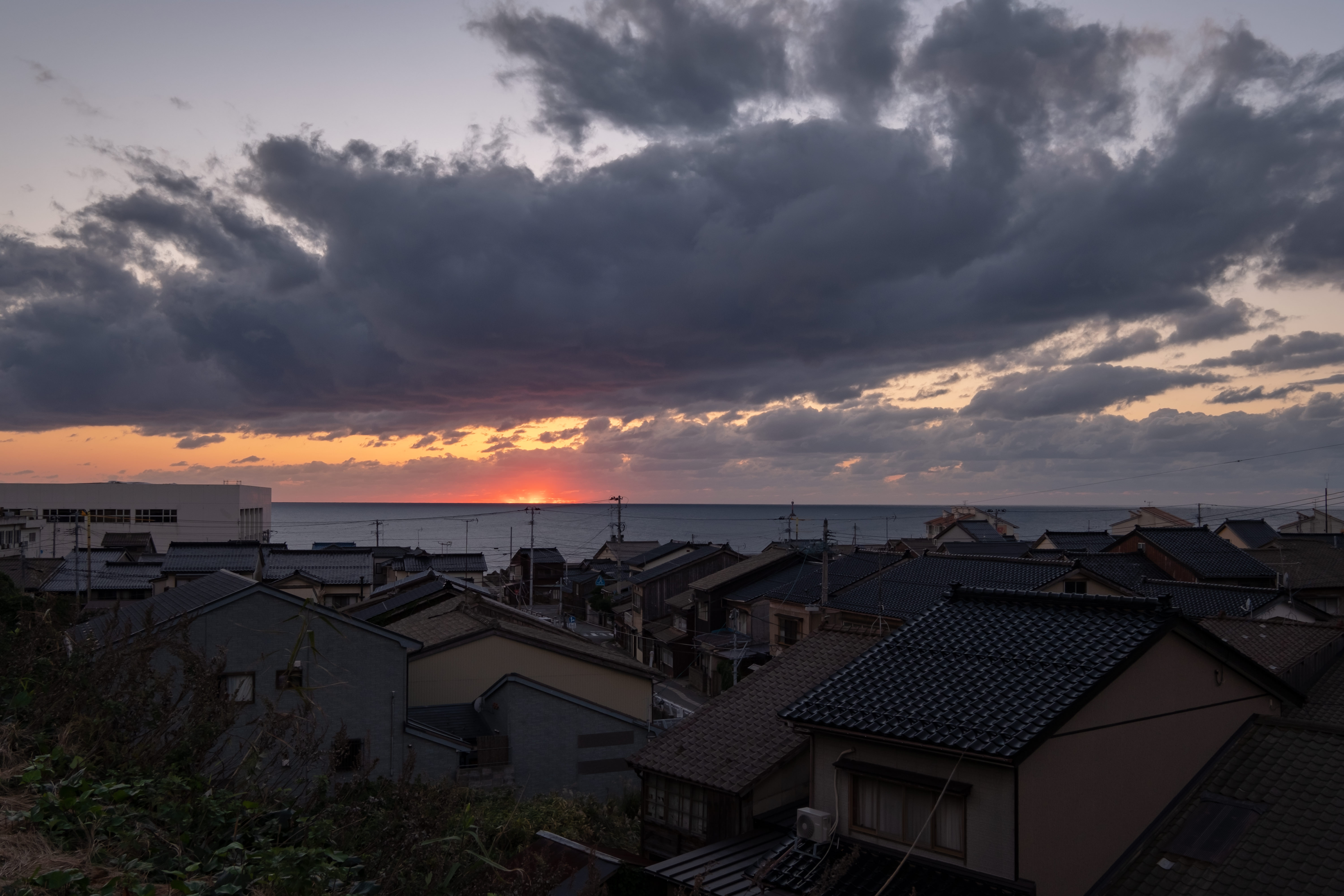 沈む夕日と海沿いの民家の写真を無料ダウンロード フリー素材 ぱくたそ