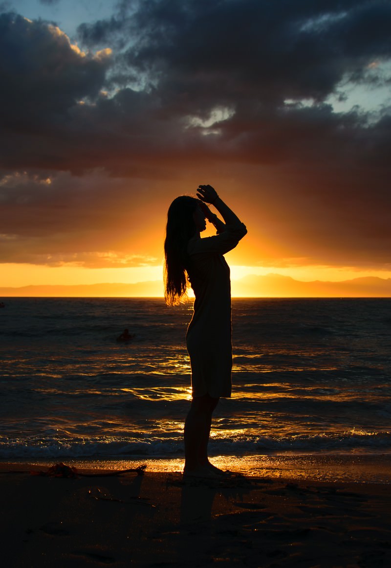 夕日をバックに砂浜で髪をかきあげようとする女性のシルエットの写真 画像 を無料ダウンロード フリー素材のぱくたそ