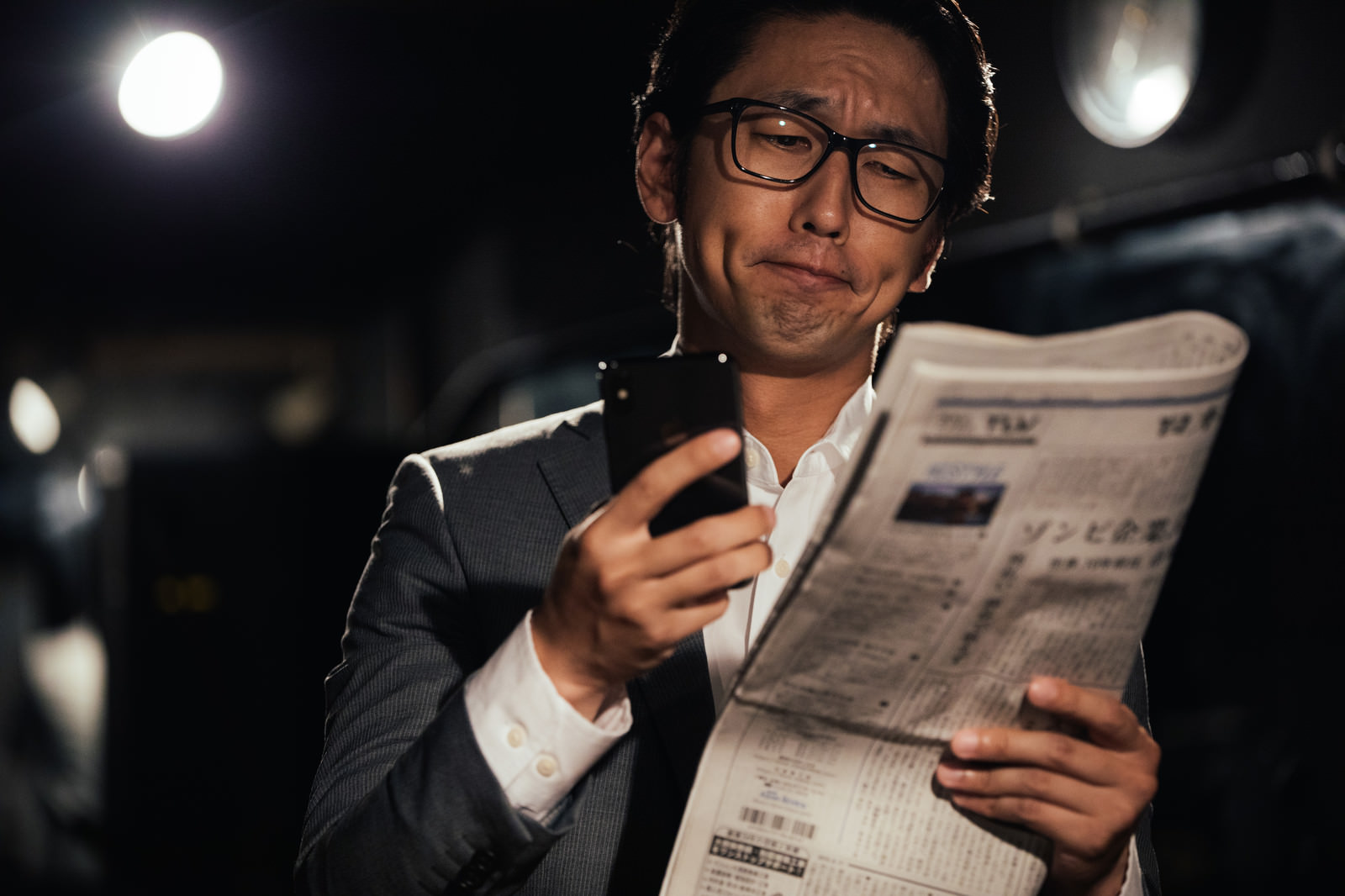 「紙面と電子版を同時にチェックするビジネスマン | フリー素材のぱくたそ」の写真［モデル：大川竜弥］