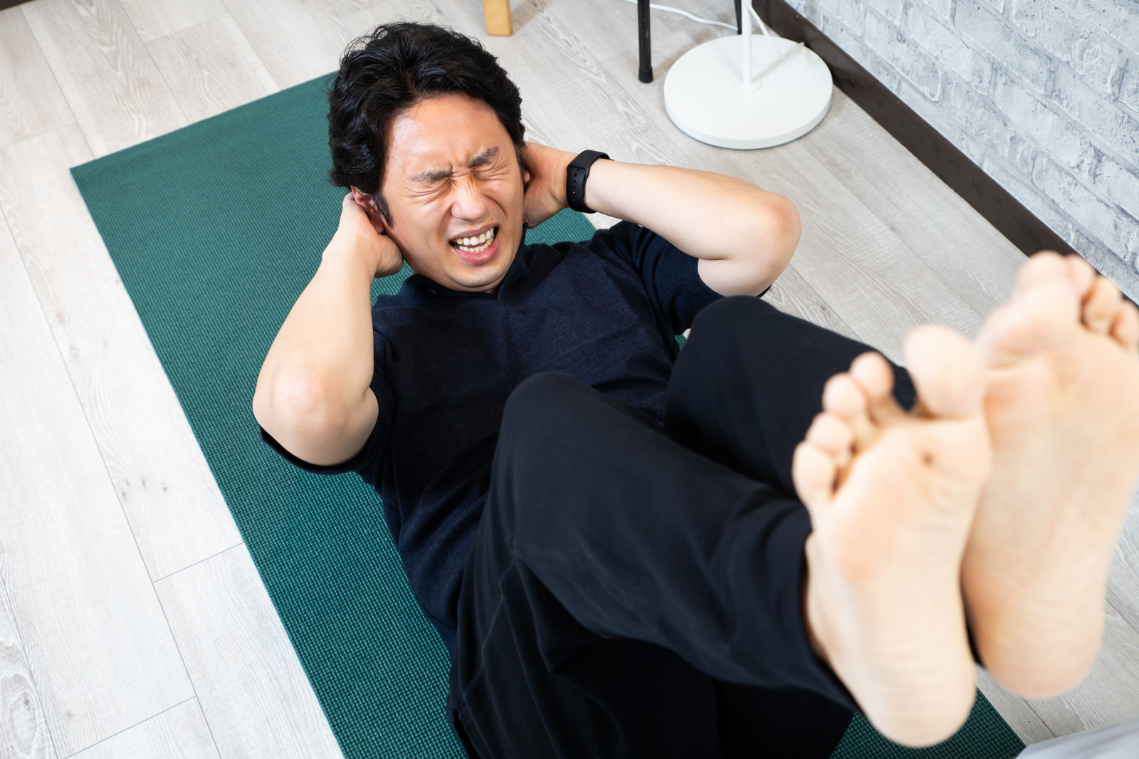 「苦しい表情で足をあげて腹筋する男性」の写真［モデル：大川竜弥］