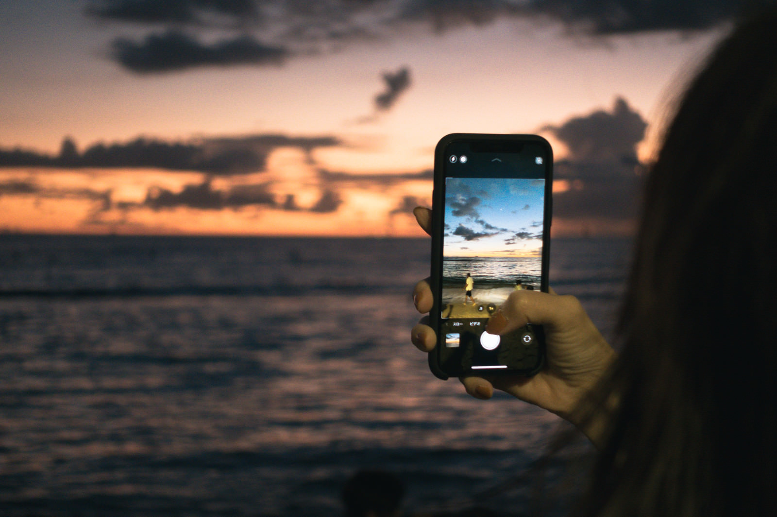 「スマホで夕焼けと波打ち際を撮影する」の写真