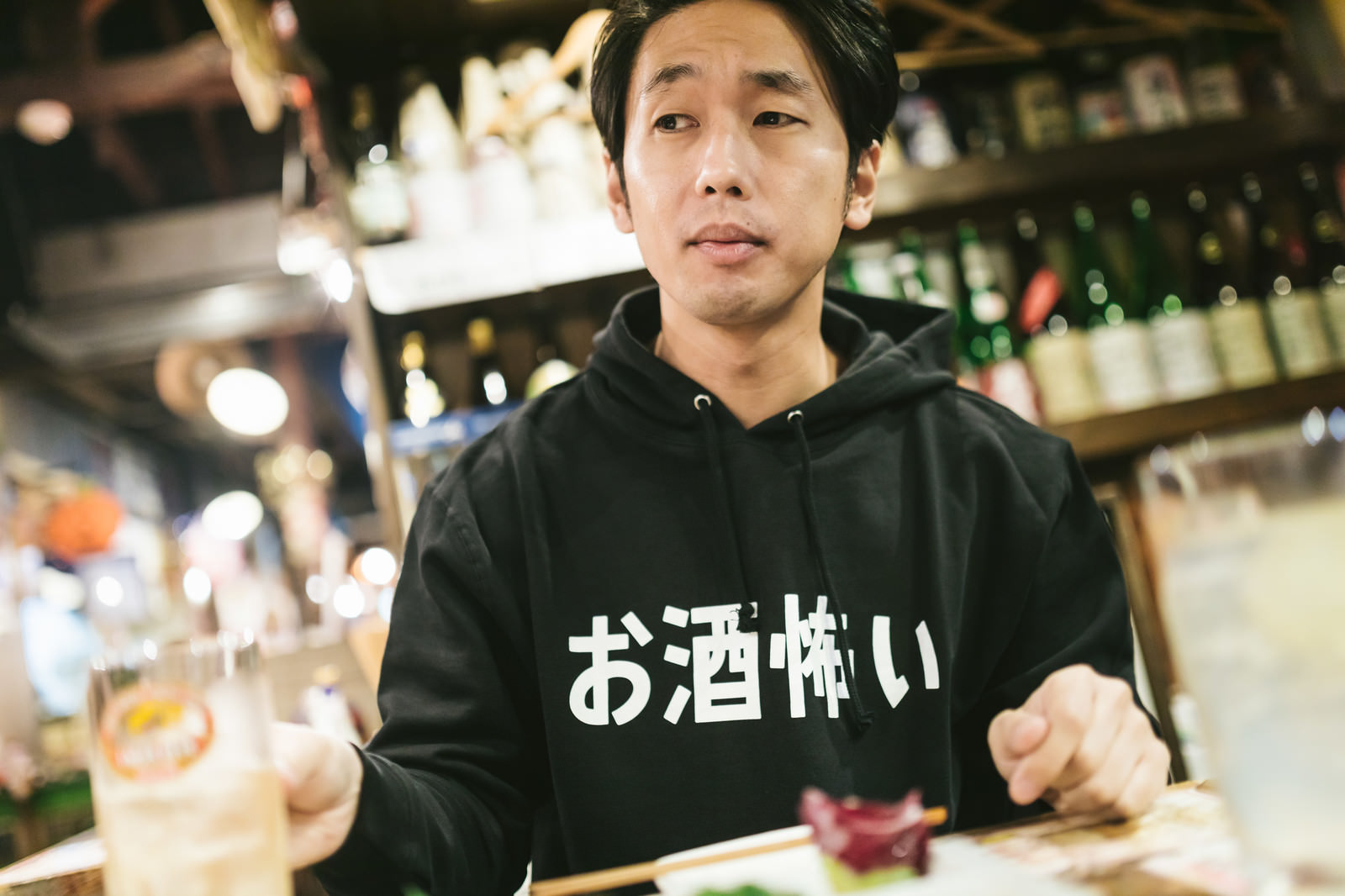 「お酒怖いと書かれたパーカーを着てお酒を飲む男性」の写真［モデル：大川竜弥］