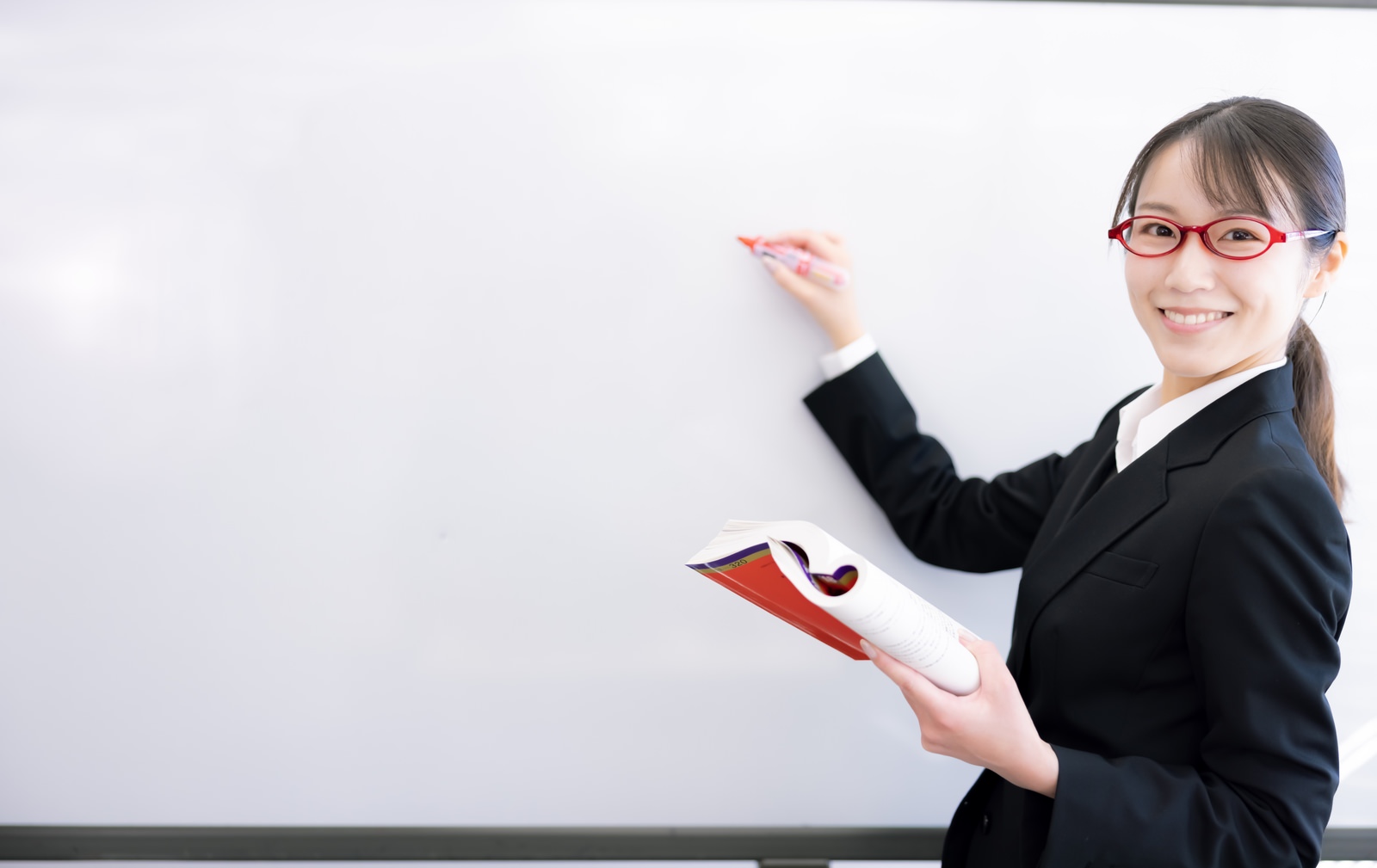 「笑顔で解答する赤い眼鏡の女性講師 | フリー素材のぱくたそ」の写真［モデル：SAKI］