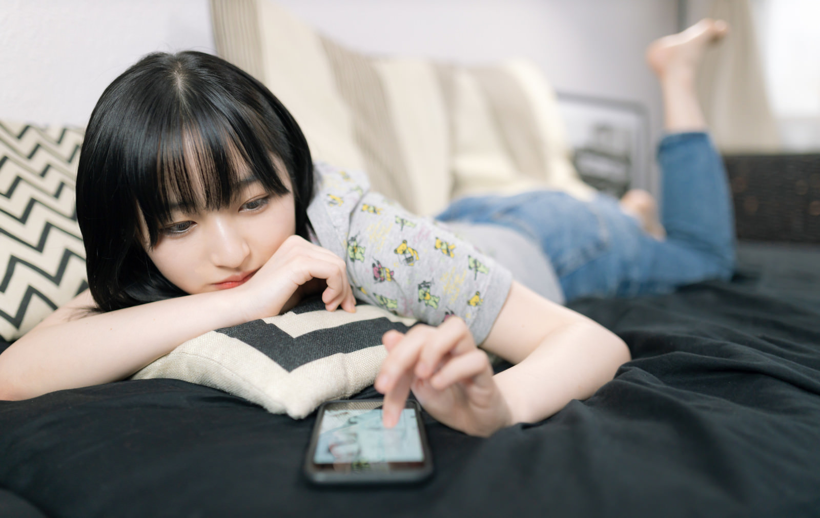 「スマホアプリに熱中する休日を過ごす女子大生」の写真［モデル：井隼そら］