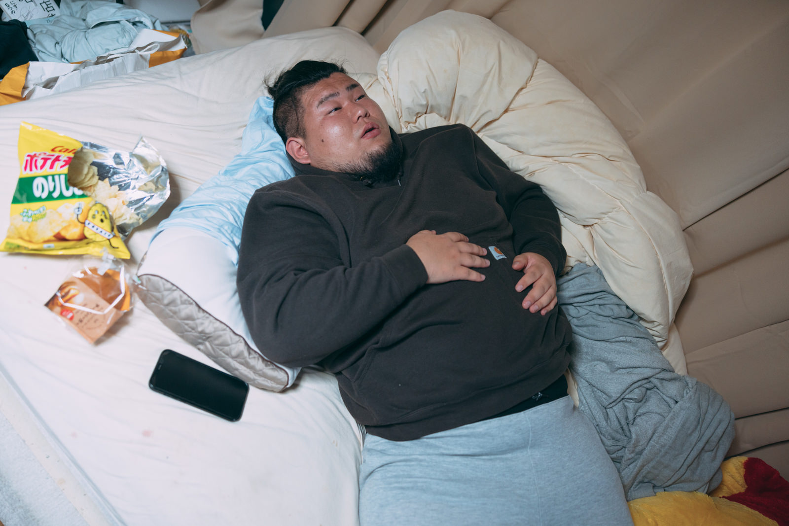 「食いすぎてベッドで横になるデブ | フリー素材のぱくたそ」の写真［モデル：ノリックス］