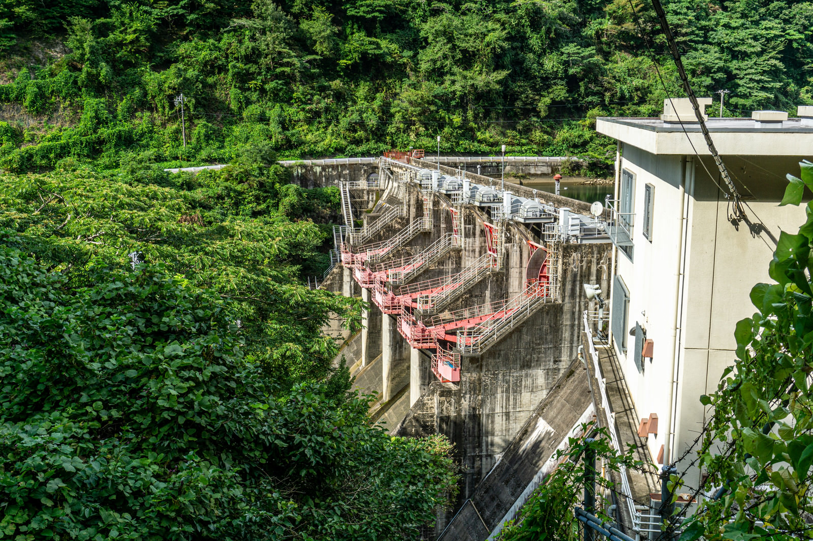 左岸の木の間から覗き見た矢作第二ダムのゲート付近の写真素材 ぱくたそ